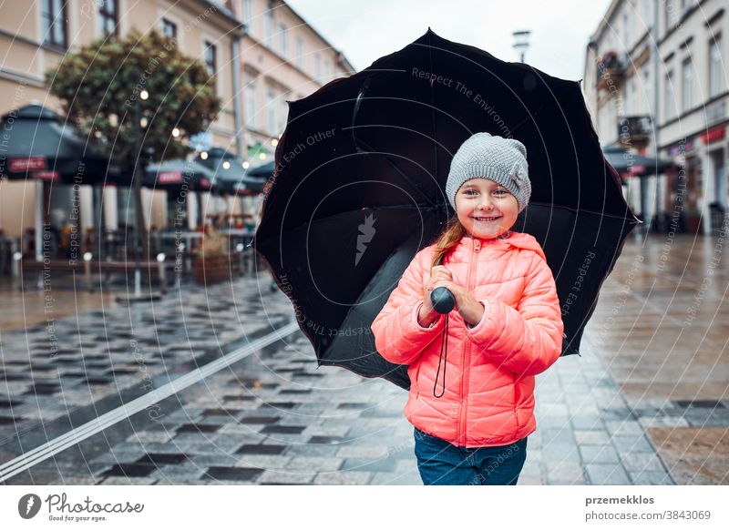 Kleines Mädchen mit großem Regenschirm in der Hand geht an einem verregneten, düsteren Herbsttag durch die Innenstadt im Freien wenig saisonbedingt fallen