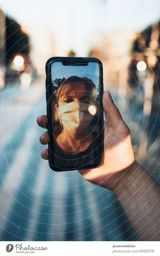 Junger Mann führt Videogespräch, während er mit der Gesichtsmaske in der Innenstadt läuft, um eine Virusinfektion zu vermeiden Anruf Pflege Kaukasier Talkrunde