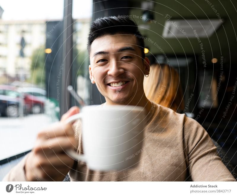 Glücklicher ethnischer Mann trinkt Kaffee im Café trinken sich[Akk] entspannen Wochenende Kaffeehaus Armsessel gemütlich Getränk männlich asiatisch heiß modern