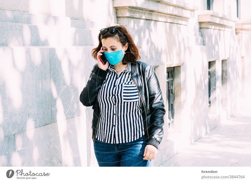 Frau mit Gesichtsmaske telefoniert, während sie die Straße entlang läuft laufen Coronavirus Sicherheit Person sprechend Erwachsener Mitteilung im Freien Handy