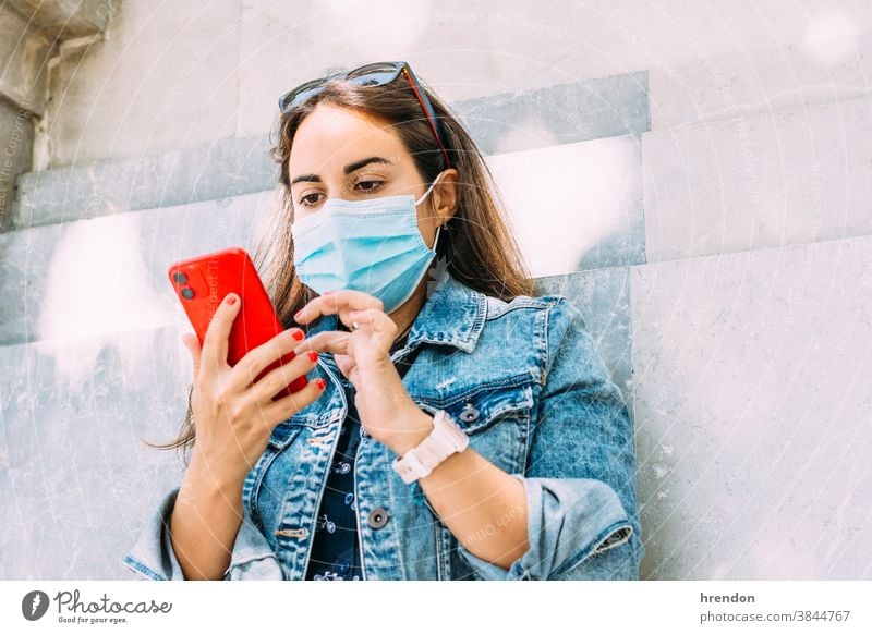 Frau mit einer Gesichtsmaske, die mit ihrem Smartphone an der Wand lehnt jung Telefon Lifestyle Lehnen Internet Mitteilung Technik & Technologie Mobile