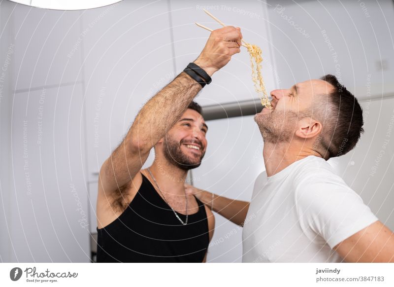 Mann gibt seinem Freund auf lustige Weise Nudeln zu essen schwul Paar Männer Homosexualität Spaghetti Spätzle Lebensmittel Essen zubereiten Küche lgbt Liebe