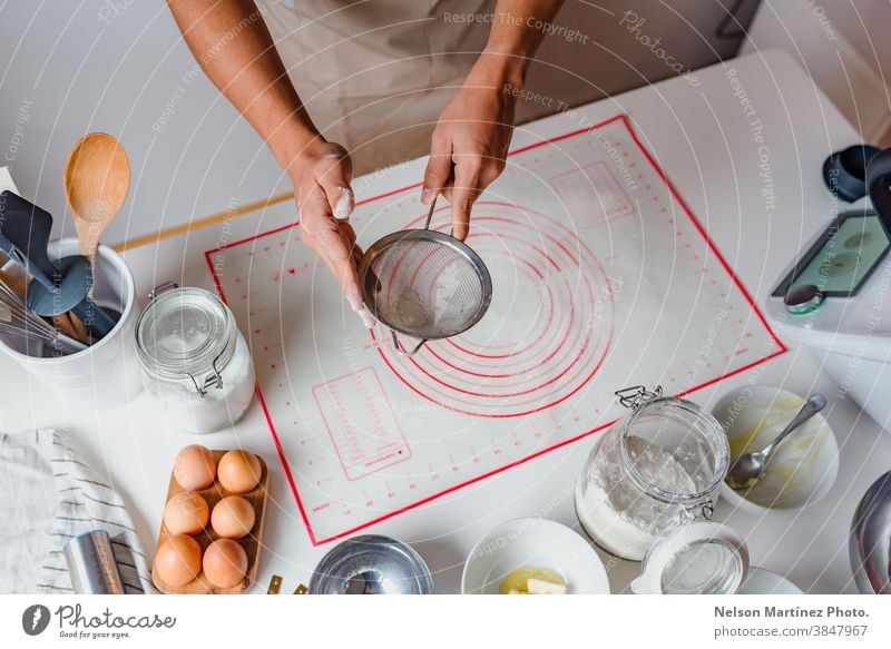 Hände eines Mannes, der Mehl durch ein Sieb auf dem Tisch sichtet. Eier Bäckerei Desserts Butter Salz Lebensmittel Essen zubereiten heimwärts hausgemacht