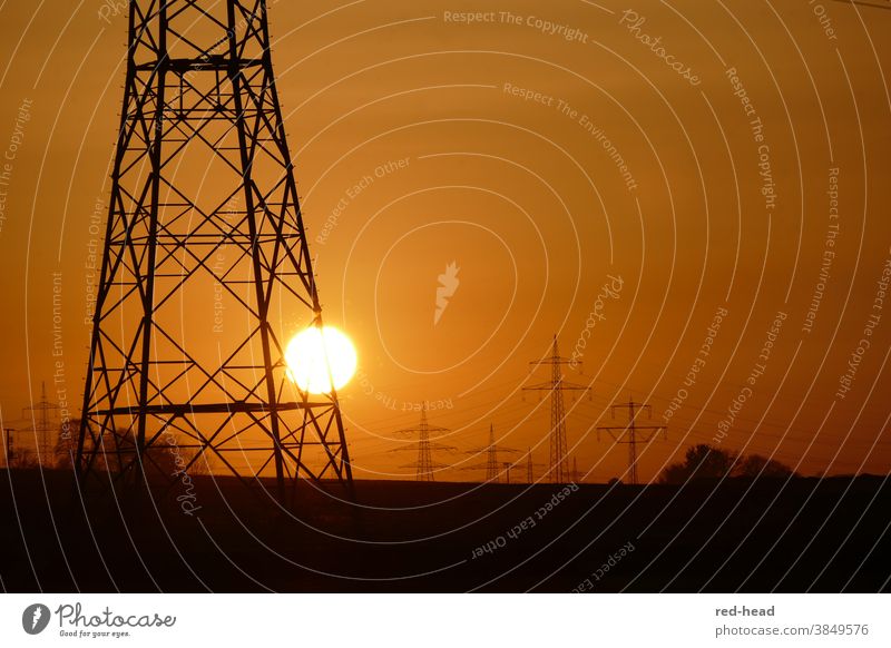 Sonnenuntergang hinter Strommast -oranger Himmel, ein Hochspannnungsmast im Vordergrund, angeschnitten, mehrere Masten im HIntergrund Hochspannungsmast