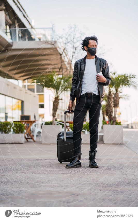 Tourist, der beim Spaziergang im Freien einen Koffer trägt. Afro-Look Mann Reisender Ausflugsziel Konzept Feiertag Tag Freude genießen Abenteuer Ferien Porträt