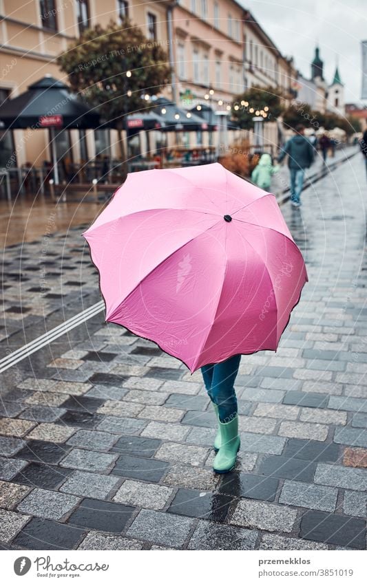 Kind, das sich hinter einem großen rosa Regenschirm versteckt und an einem regnerischen, düsteren Herbsttag in der Innenstadt spazieren geht regnet im Freien