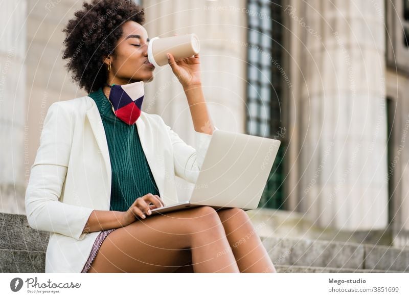 Geschäftsfrau, die ihren Laptop im Freien benutzt jung Afro-Look Business Frau urban Straße Erfolg Gerät korporativ Information Kaffee Gesichtsmaske Schutzmaske