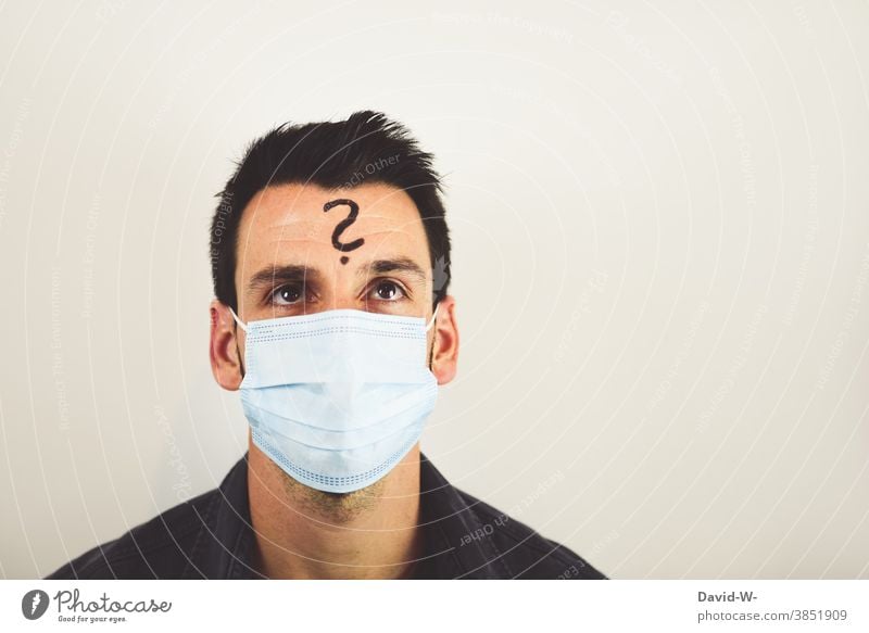 fragender Mann mit Atemschutzmaske / Mundschutz und Fragezeichen auf der Stirn Corona denken wieso ? nachdenklich skeptisch Zweifel pandemie Quarantäne