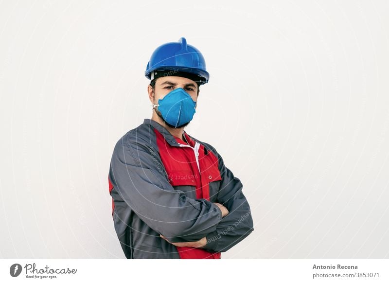 Attraktiver Arbeiter Mann mit Gesichtsmaske zum Schutz schaut in die Kamera covid-19 Mundschutz Uniform Sicherheit Pandemie Virus weißer Hintergrund Wand