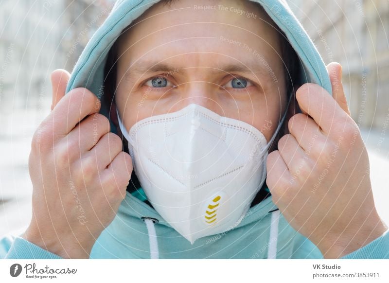 Nahaufnahme eines europäischen Mannes, der sein Gesicht mit einer Atemschutzmaske schützt, Kapuzenpulli trägt, draußen auf der Straße posiert, ernsthaft in die Kamera schaut, verhindert Coronavirus oder Covid-19, Grippe. Straße während der Quarantäne