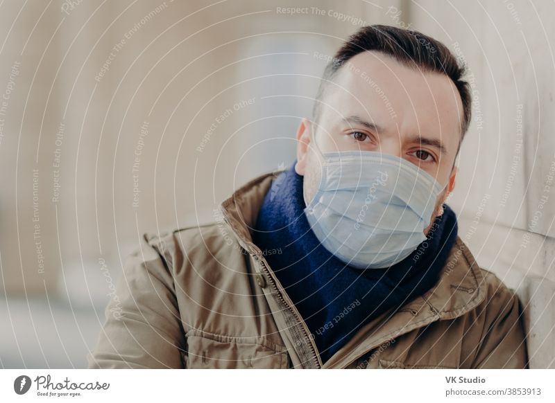 Freiluftaufnahme eines jungen europäischen Mannes mit Coronavirus-Symptomen, trägt schützende Operationsmaske, versucht sich vor Viren und Infektionen zu schützen, muss zum Arzt. Problem der Straßen- und Luftverschmutzung