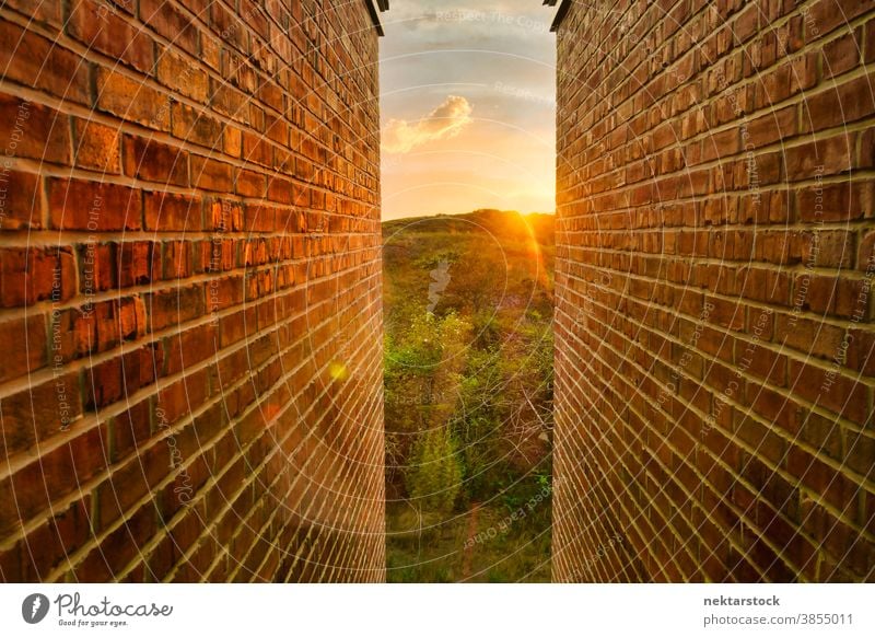 Goldener Sonnenaufgang und Landschaft zwischen Backsteinmauern Wand Baustein eng golden Eröffnung Licht am Ende des Tunnels Gabellandschaft Konzept Hoffnung