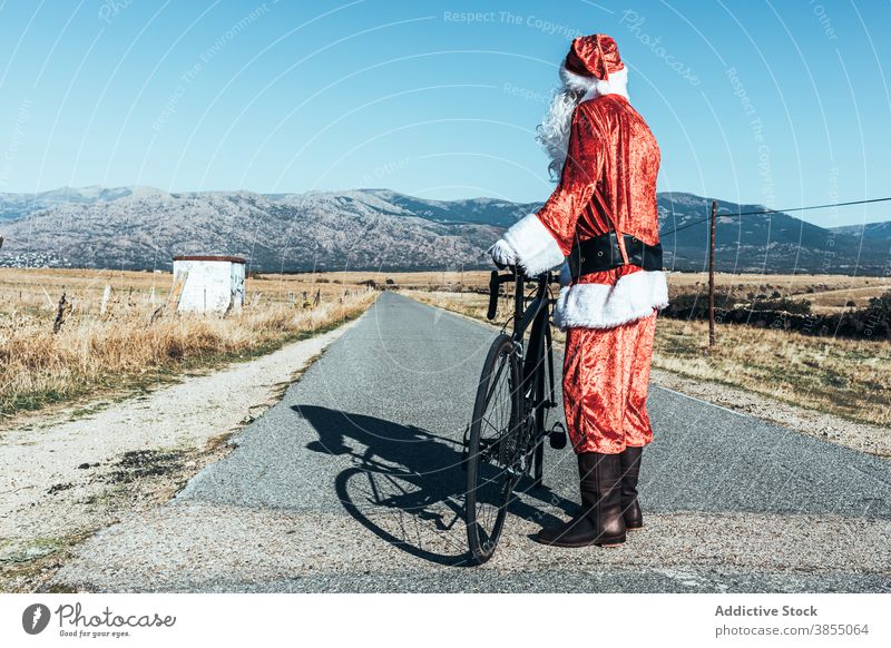 Anonymer Weihnachtsmann in der Nähe von Fahrrad auf der Straße auf dem Lande Landschaft sich[Akk] entspannen Fahrbahn Fahrzeug Weihnachtsmütze männlich Vollbart