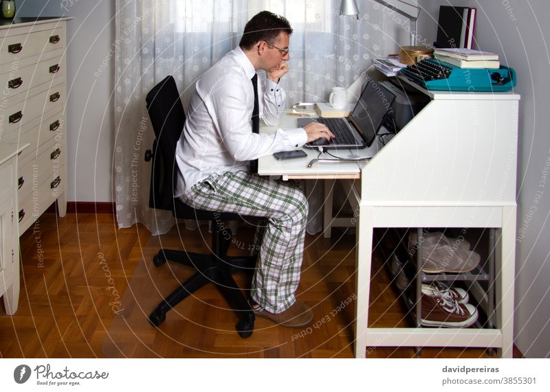 Mann bei der Telearbeit mit Hemd, Krawatte und Pyjamahose von zu Hause aus arbeiten Coronavirus Seuche Quarantäne soziale Distanzierung Laptop Internet