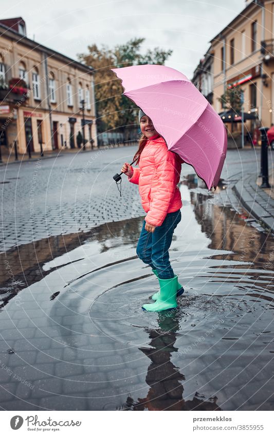 Kleines Mädchen mit großem rosa Regenschirm in der Hand geht an einem verregneten, düsteren Herbsttag durch die Innenstadt im Freien wenig saisonbedingt fallen