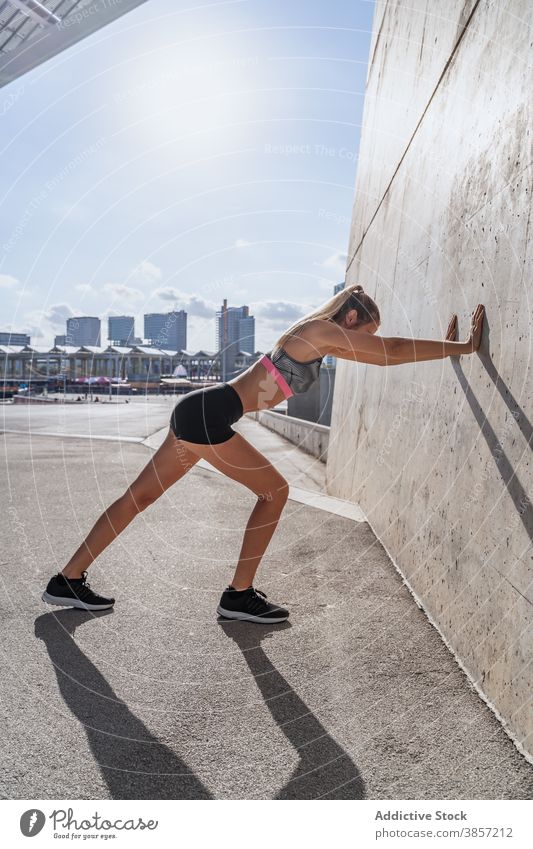 Sportlerin streckt die Beine in der Nähe der Gebäudewand Dehnung Wand fettarm Übung Aufwärmen aktiv Training Großstadt Frau Athlet Fitness Sportbekleidung