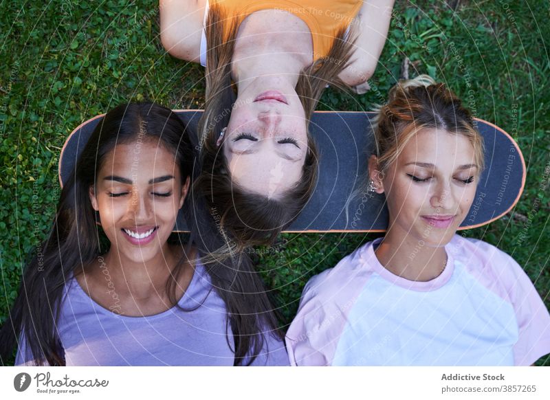 Junge Frauen mit Skateboard liegend auf grünem Gras Freundin Park Kälte Lügen Sommer Glück heiter Zusammensein ruhen Teenager rassenübergreifend multiethnisch