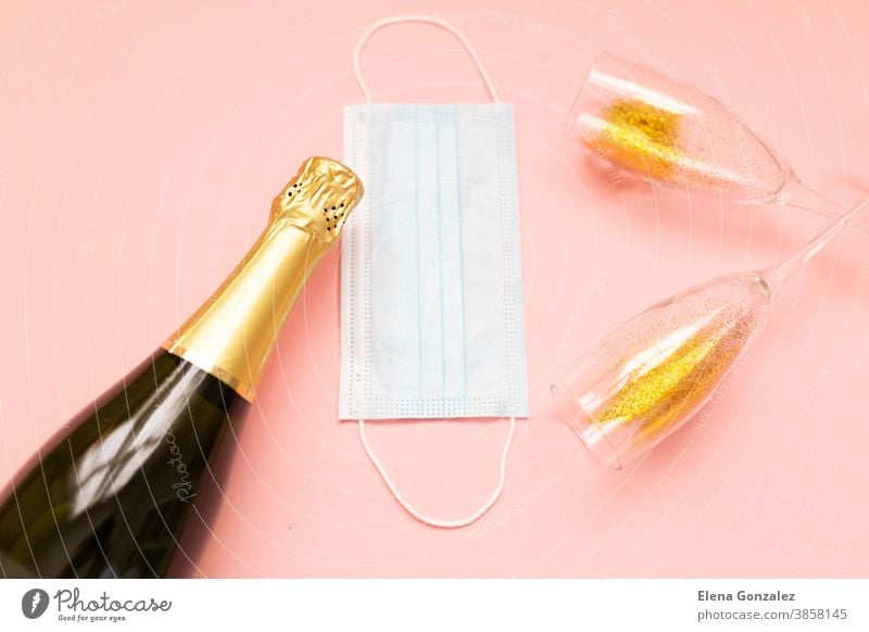 Flasche mit Champagner-Gesichtsmaske und Gläsern mit Goldglitzer auf rosa Hintergrund. Party-Dekoration. Weihnachts-, Geburtstags- oder Hochzeitskonzept. Flachgelegt. Festlich, Getränk. Neujahr 2021-Feier.