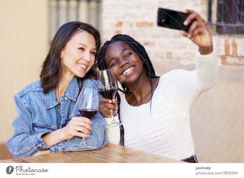Zwei Frauen, die bei einem Glas Wein ein Selfie mit einem Smartphone machen. Bar im Freien rassenübergreifend Fröhlichkeit Mädchen Freundschaft Glück Lächeln