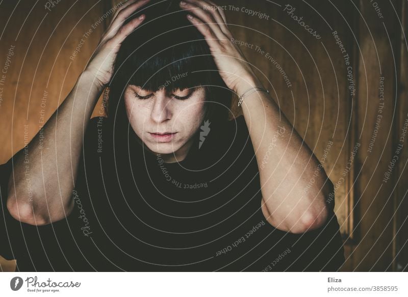 Portrait einer Frau, die nachdenklich, niedergeschlagen dasitzt und den Kopf in den Händen hält traurig Hände am Kopf depressiv verzweifelt betrübt Trübsal