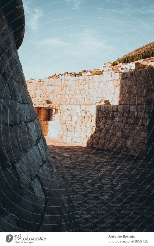 Von Mauern umgebener, schlingenförmiger Kreisbereich um den Turm der Burg Minceta in der Altstadt von Dubrovnik, der von starkem Sonnenlicht beleuchtet wird und mit Schatten Formen bildet