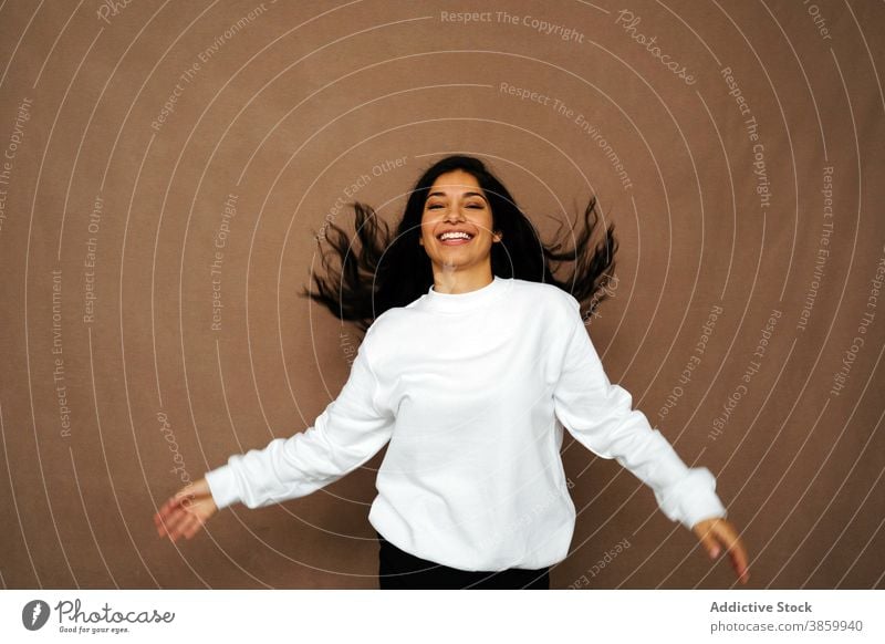 Erfreute Frau mit fliegenden Haaren im Studio fliegendes Haar Spaß haben Lachen Atelier weiß Sweatshirt lässig Stil heiter ethnisch genießen modern positiv