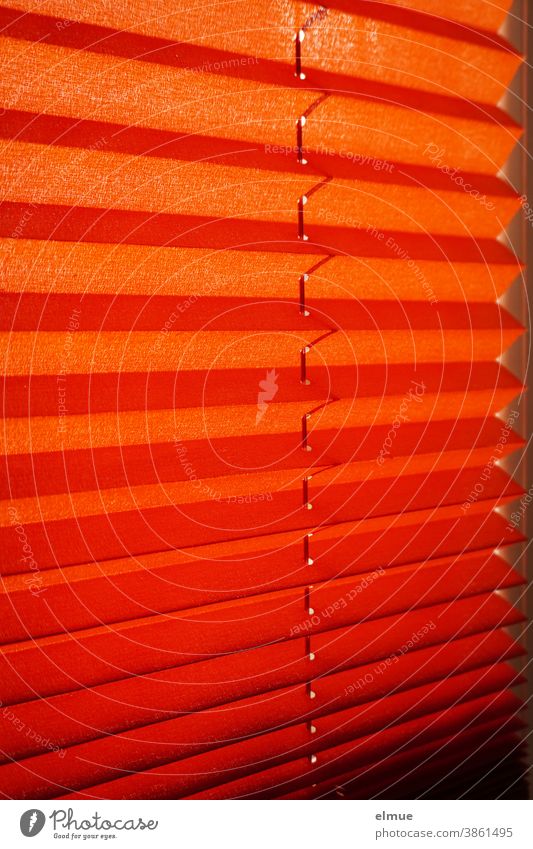 orangefarbene Plisseejalousie vor einem Fenster als Sonnenschutz / Lichtschutz / Sichtschutz Jalousie Lamellen innen wohnen Rollo Fenstervorhang