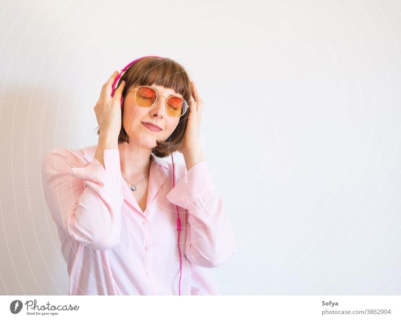 Junge glückliche Frau in rosa Hemd mit Kopfhörern Mode Sonnenbrille Lächeln Musik zuhören vertieft engagiert Telefon Glück jung Farbe Lifestyle benutzend