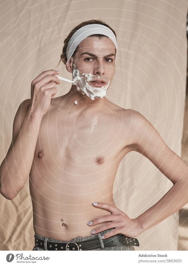 Androgyner junger Mann rasiert Gesicht Rasieren androgyn Transgender Hygiene Pflege vorbereiten Rasierer ohne Hemd schlank männlich Maniküre schäumen Hautpflege
