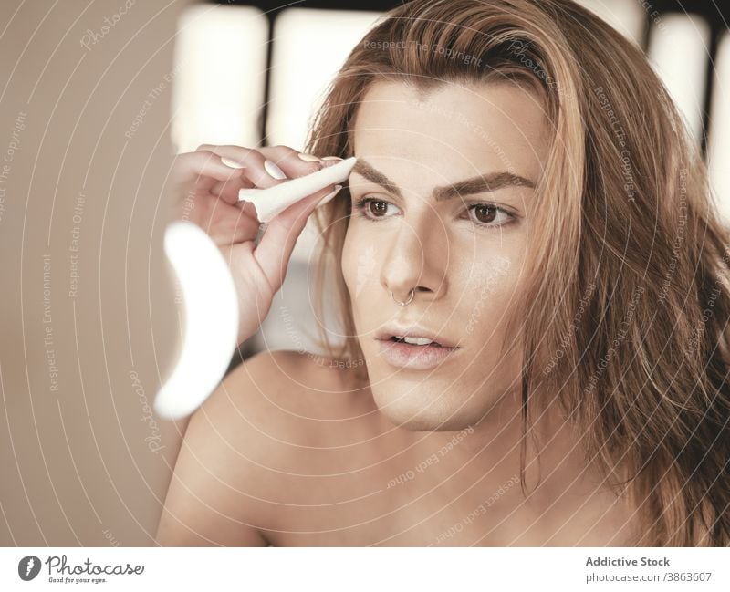 Androgyner Mann mit langen Haaren beim Auftragen von Make-up bewerben Atelier androgyn Schönheit Fundament Spiegel Transgender Vorschein männlich jung Model