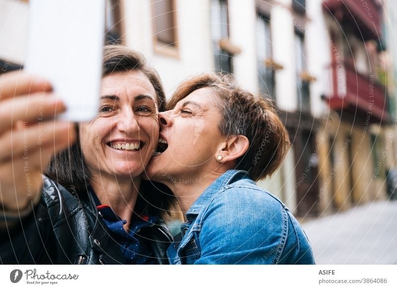 Glückliches lesbisches Paar mittleren Alters mit lustigem Egoismus lgbtq schwul mittleres Alter 40 50 Lachen Selfie Smartphone Selbstportrait Lächeln Umarmen