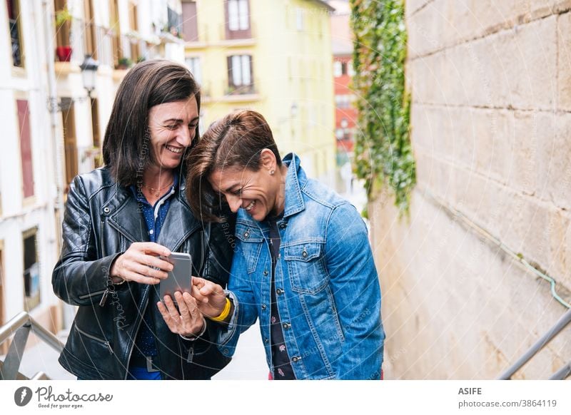 Lustiges lesbisches Paar mittleren Alters, das über etwas im Mobiltelefon lacht lgbtq schwul mittleres Alter 40 50 Lachen Selfie Smartphone Selbstportrait
