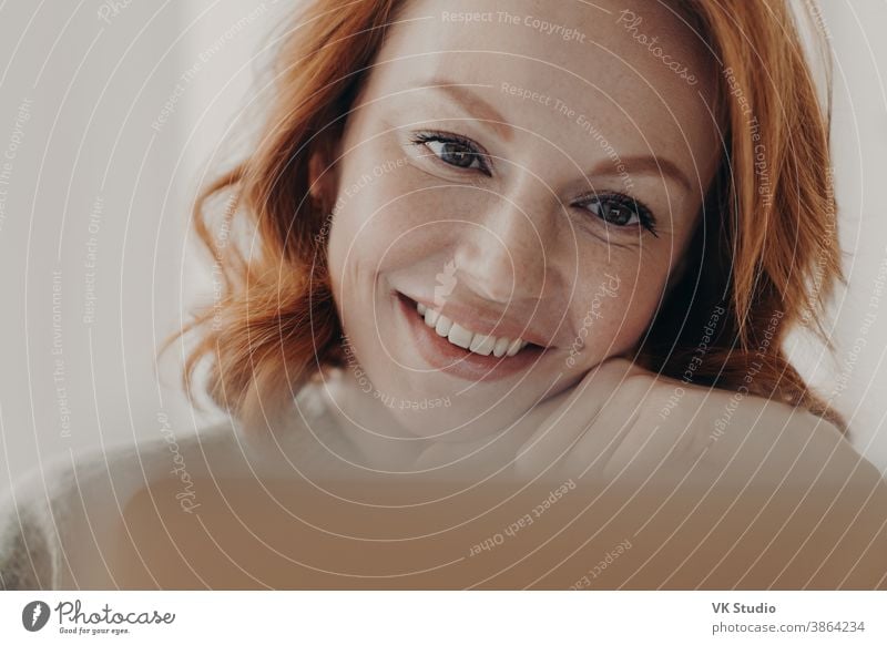 Nahaufnahme einer positiv gestimmten rothaarigen Frau mit sommersprossiger Haut und zahnartigem Lächeln, konzentriert am Bildschirm eines Laptop-Computers, zufrieden mit dem Online-Geschäft, prüft eingegangene Nachricht, hat einen Fernjob