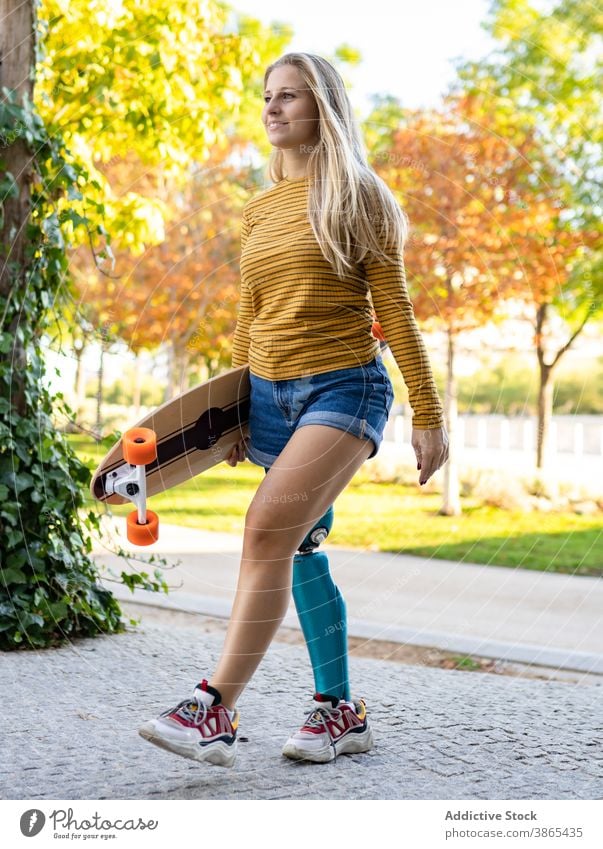 Lächelnde Frau mit Longboard zu Fuß auf der Straße Bein Prothesen Bionik Skater künstliches Glied Spaziergang deaktivieren urban Skateboard Amputierte Stadt