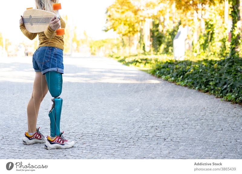 Schlanke Frau mit Longboard und Beinprothese auf der Straße Prothesen Bionik Skater künstlich Glied deaktivieren urban Skateboard Stadt modern Sonnenlicht