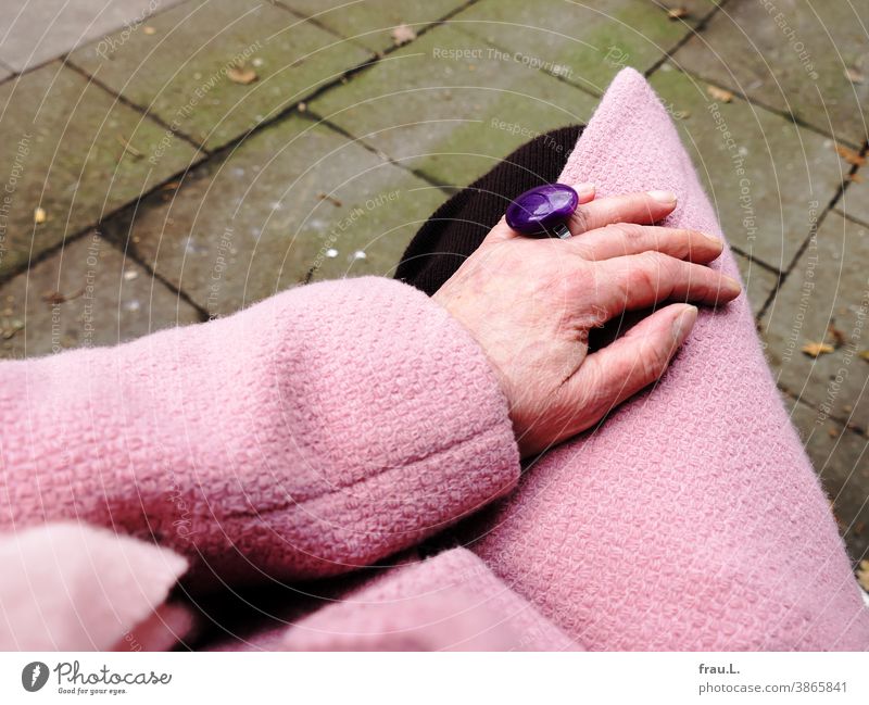 Alte Frauenhand mit rosa Mantel, rosa Schal und violettem Ring sowie kleiner Katerkratzwunde Hand Mensch Strickrock Mode Fingerring Modeschmuck Fußweg sitzen