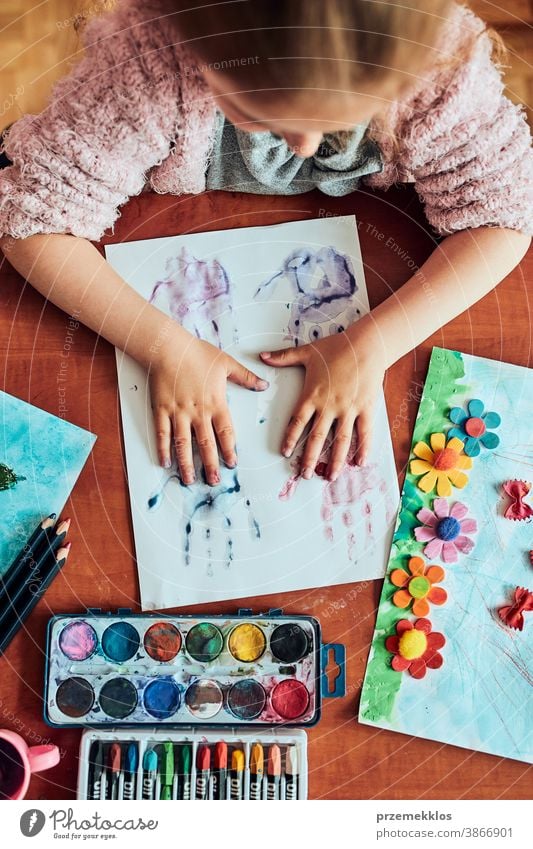 Kleines Mädchen im Vorschulalter, das mit bunten Farben und Buntstiften ein Bild malt. Kind, das während eines Kunstunterrichts im Klassenzimmer Spaß beim Malen eines Bildes hat