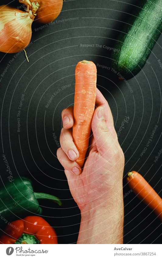Hand greift eine Karotte umgeben von Gemüse mit einem schwarzen Tisch kulinarisch Küche Essen zubereiten Schneidebrett Vorbereitung Messer Lebensmittel hölzern