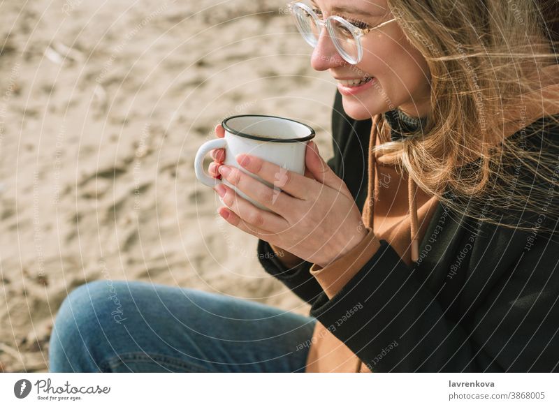 Porträt einer jungen erwachsenen Frau mit Emaillebecher mit heißem Getränk am Strand sitzend Becher Tasse Herbst Winter trinken Glück Tee Lifestyle Lächeln