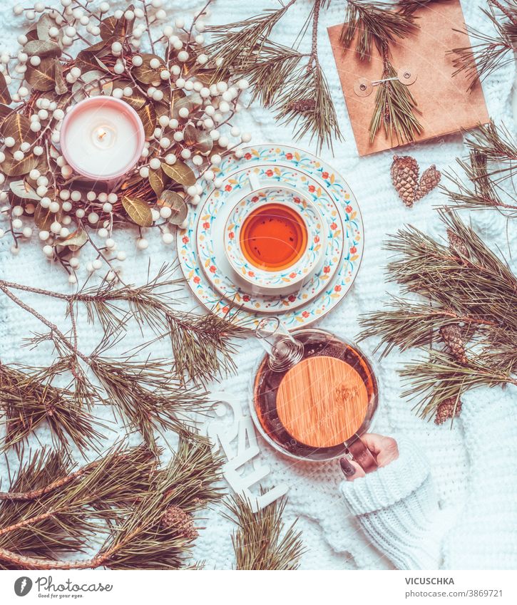 Winter und Weihnachten Lebensstil. Frau hält Teekanne auf weißer Strickdecke mit Tasse Tee, Weihnachtskranz und Tannenzapfen und -zweigen in der Hand. Ansicht von oben