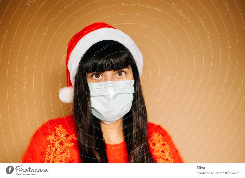 Junge Frau in weihnachtlicher Kleidung trägt Mundschutz und eine Nikolausmütze. Weihnachten während der Corona Pandemie. Maske Einwegmaske Weihnachtsstimmung