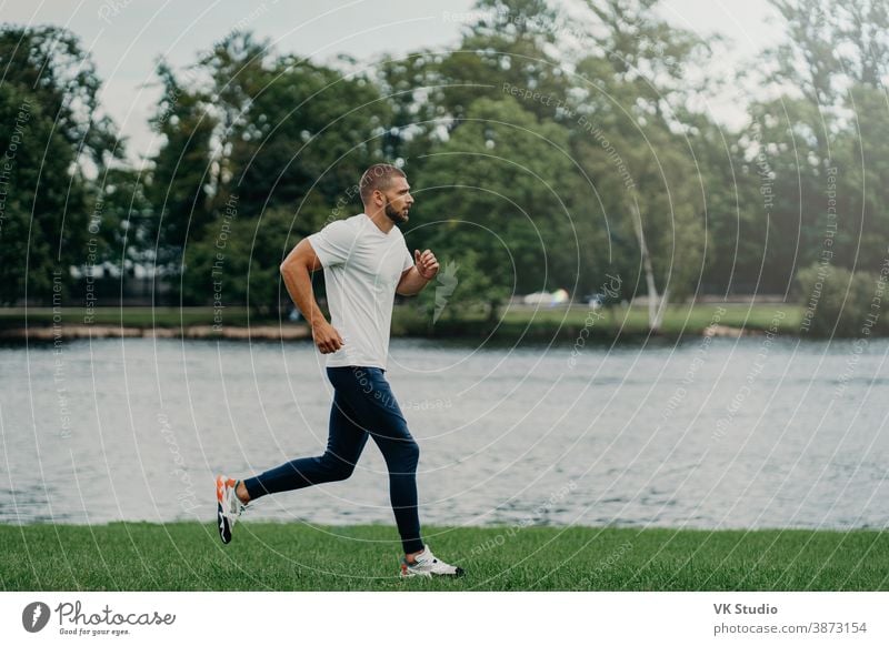 Sportler bärtiger Mann rennt durch schöne Landschaft, demonstriert Ausdauer, in aktive Kleidung gekleidet, geht am Fluss joggen, atmet frische Luft. Sport-, Bewegungs-, Fitness- und Workoutkonzept