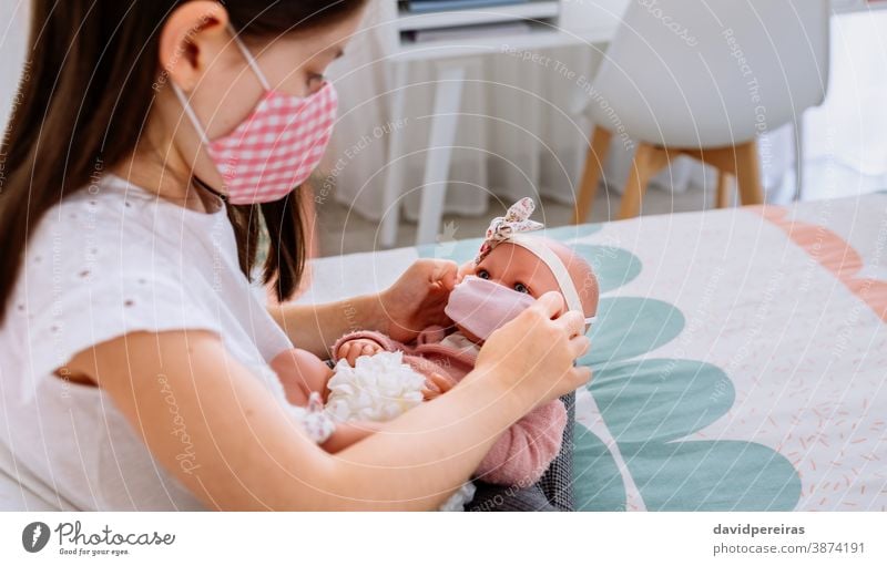 Mädchen mit Maske setzt ihrer Puppe eine kleine Maske auf Spielen Steckmaske Gesicht covid-19 Coronavirus-Erzeugung Pflege Menschen Sperrung Kind Frau