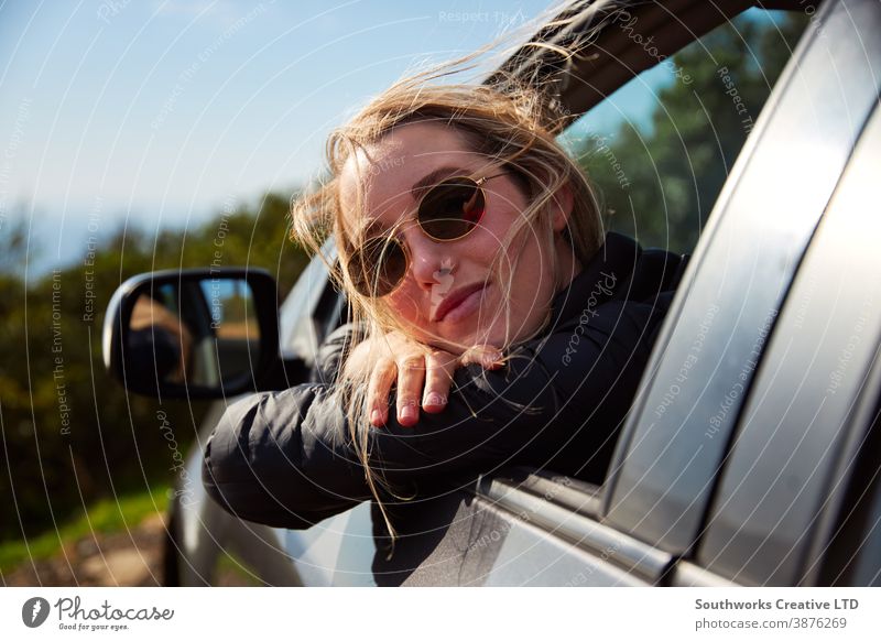 Junge Frau auf Roadtrip-Urlaub aus dem Mietwagenfenster gelehnt mit Berglandschaft im Rücken Autoreise Autovermietung Feiertag Junge Frauen PKW fahren Fahrer