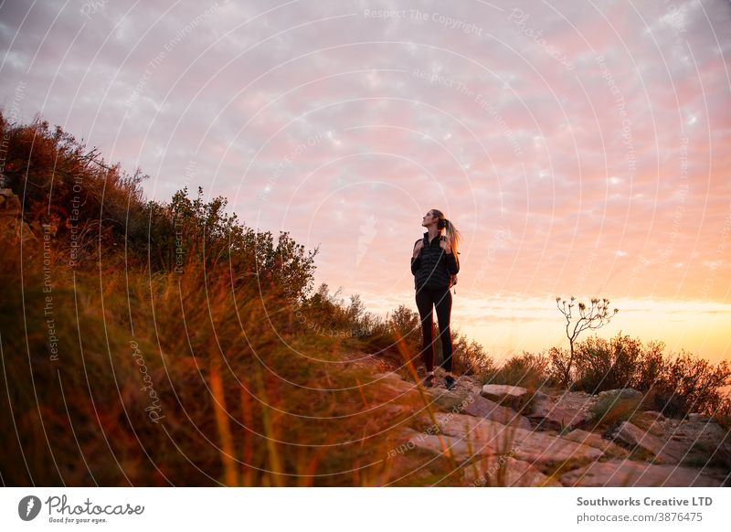 Frontansicht einer jungen Frau mit Rucksack, die bei Sonnenuntergang zu einer Wanderung auf dem Landweg aufbricht Abenteuer Sonnenaufgang Junge Frauen wandern