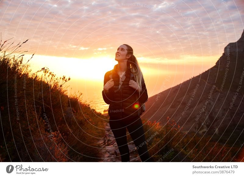 Frontansicht einer jungen Frau mit Rucksack, die bei Sonnenuntergang zu einer Wanderung entlang des Küstenweges aufbricht Abenteuer Sonnenaufgang goldene Stunde