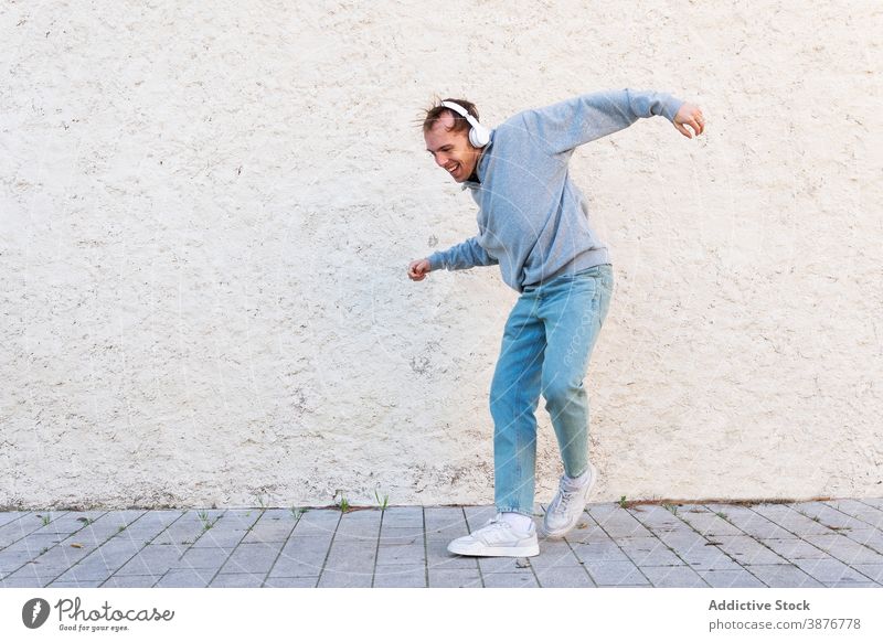 Optimistischer Mann mit Kopfhörer tanzt auf der Straße Tanzen heiter Musik Hipster Glück Energie urban jung männlich lässig Wand zuhören Lifestyle Klang Gesang