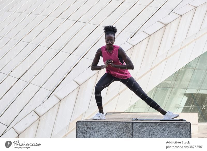 Seriöse schwarze Läuferin, die in der Stadt trainiert Großstadt Training Seitenlonge Übung Sportlerin Dehnung Bein Aufwärmen Frau ethnisch Afroamerikaner