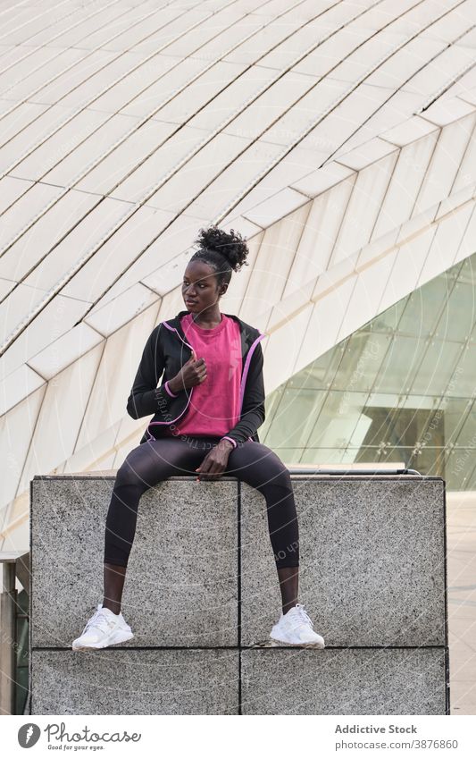 Ernste schwarze Sportlerin sitzt auf Stein Grenze in der Stadt Athlet Bestimmen Sie selbstbewusst Läufer Straße Großstadt ernst passen Sportbekleidung Frau