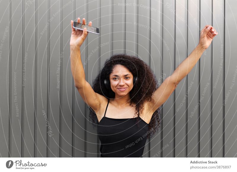 Optimistische schwarze Frau, die auf der Straße Musik hört zuhören Kopfhörer meloman genießen Afro-Look Frisur krause Haare Smartphone ethnisch Afroamerikaner